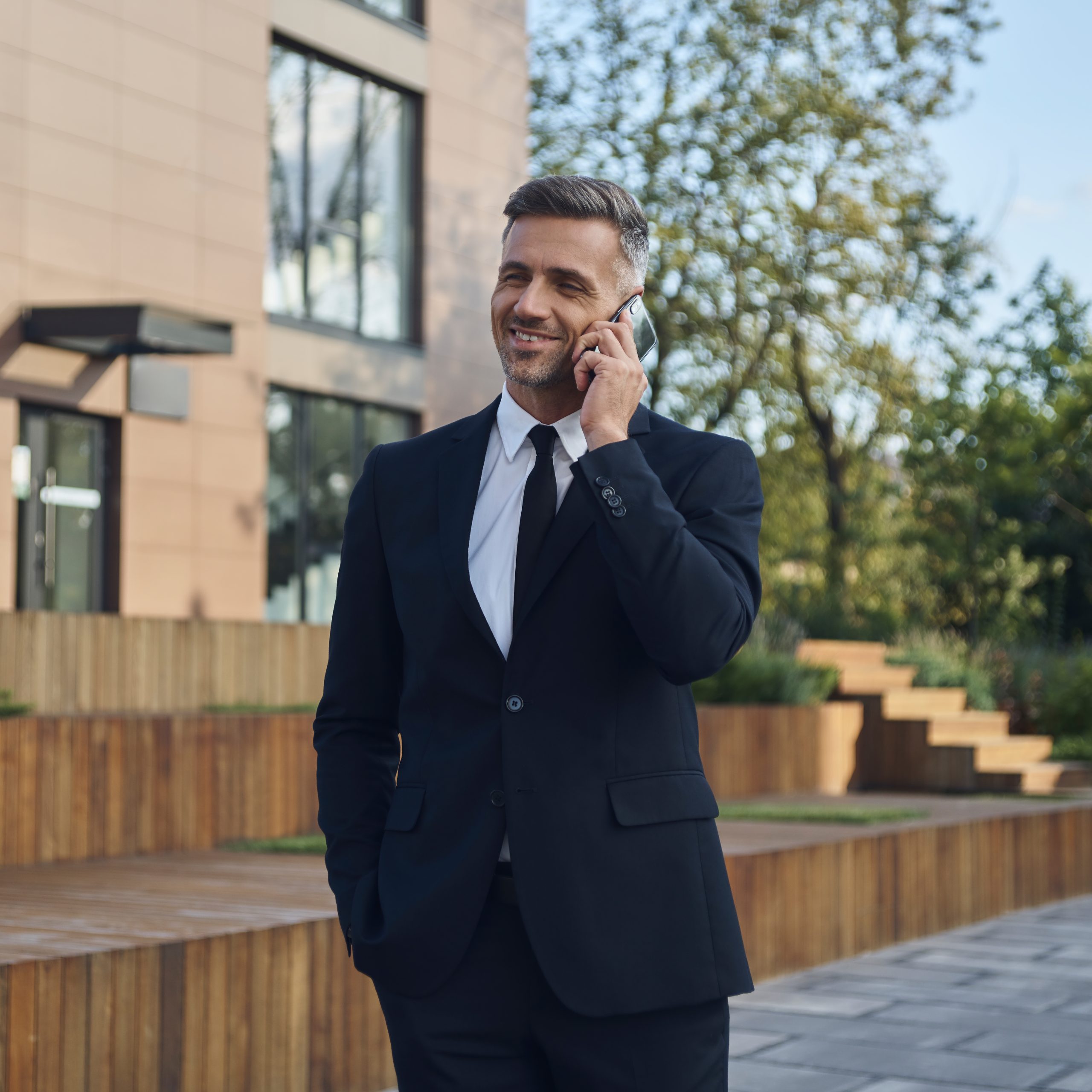 Confident mature businessman talking on mobile phone while standing outdoors near office building