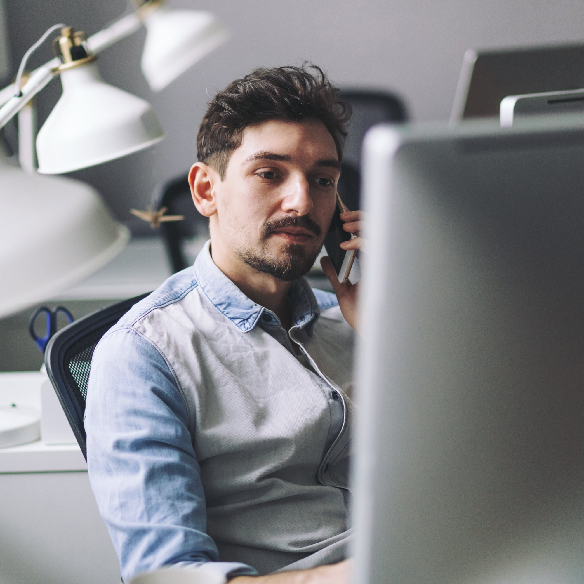 Young man working on computer and using mobile phone while sitting at his working place in office